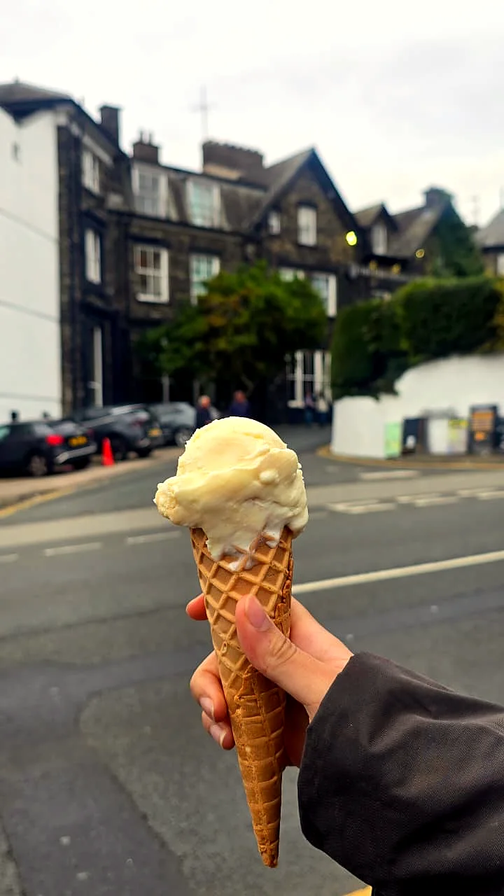 A hand holding an ice cream cone on a grey street.