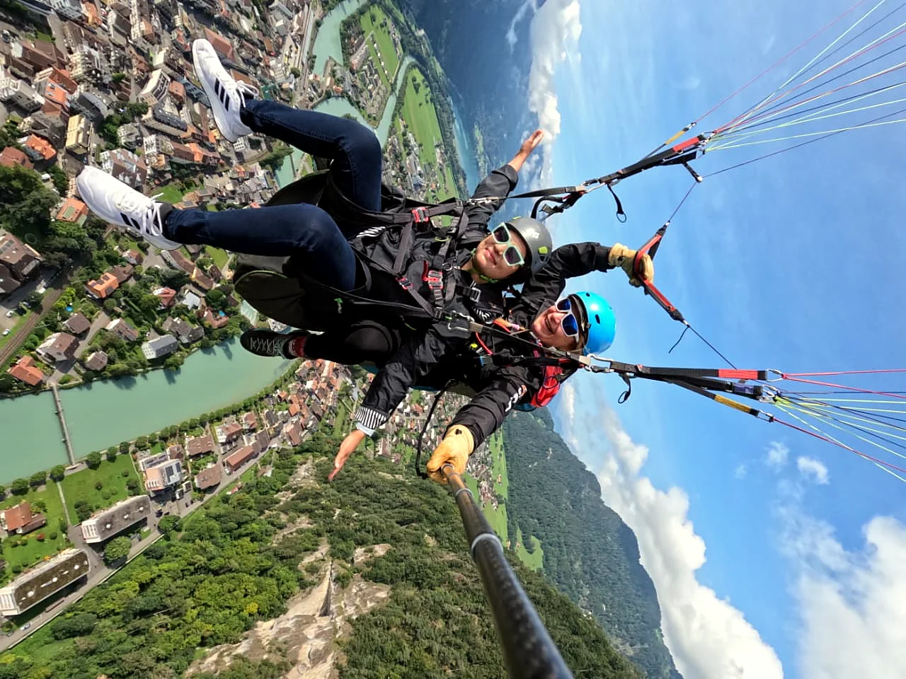Tandem paragliding high above Interlaken, the river and green hills below.